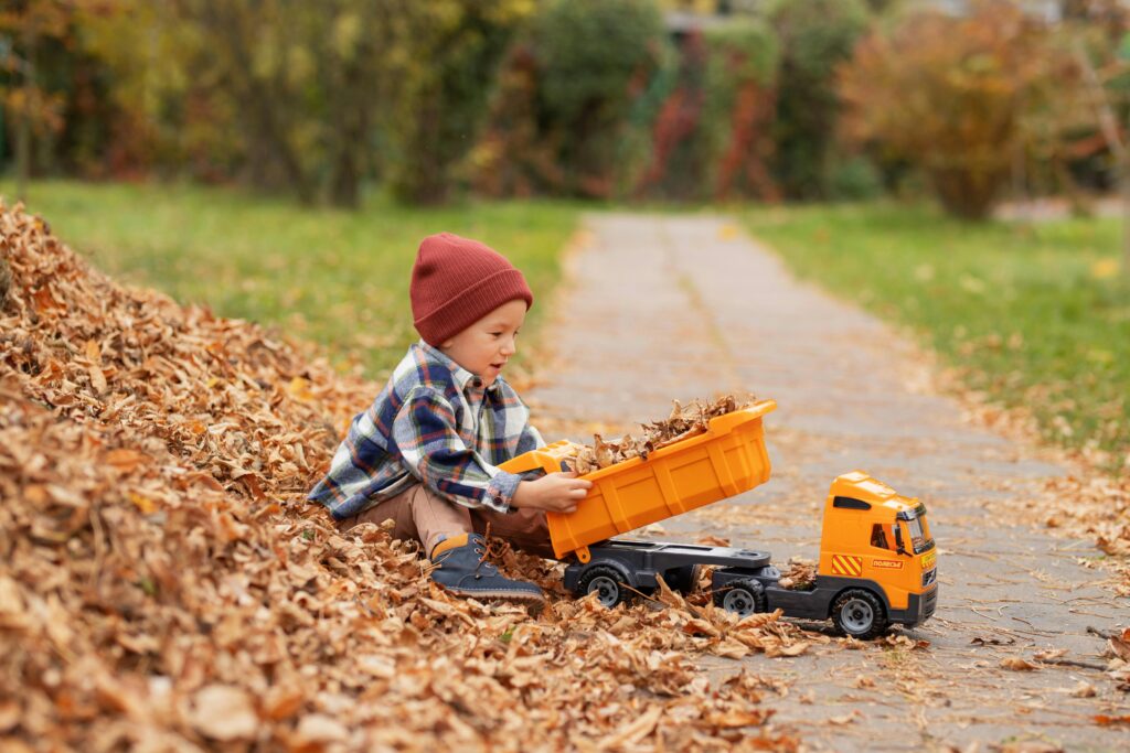 a child sitting in a pile of leaves playing with a toy truck